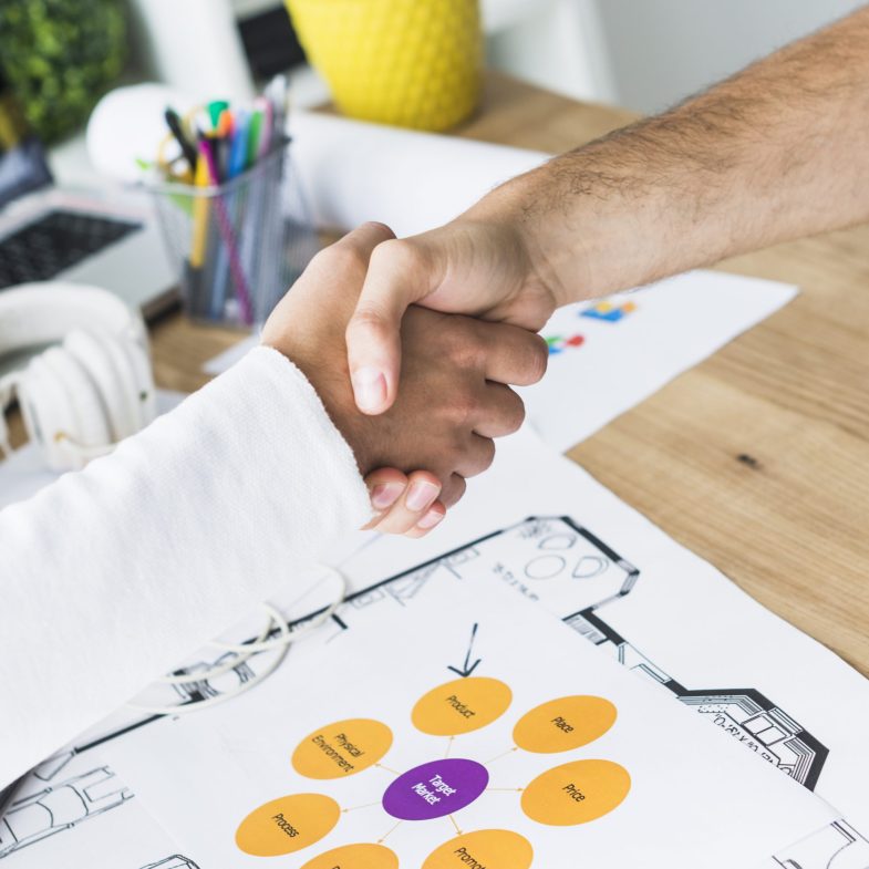 close up two businessmen shaking hands desk scaled e1759453220200